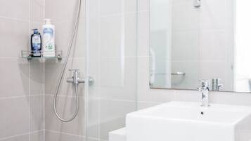 Un bany modern amb una cabina de dutxa de vidre, un lavabo blanc i un mirall damunt.