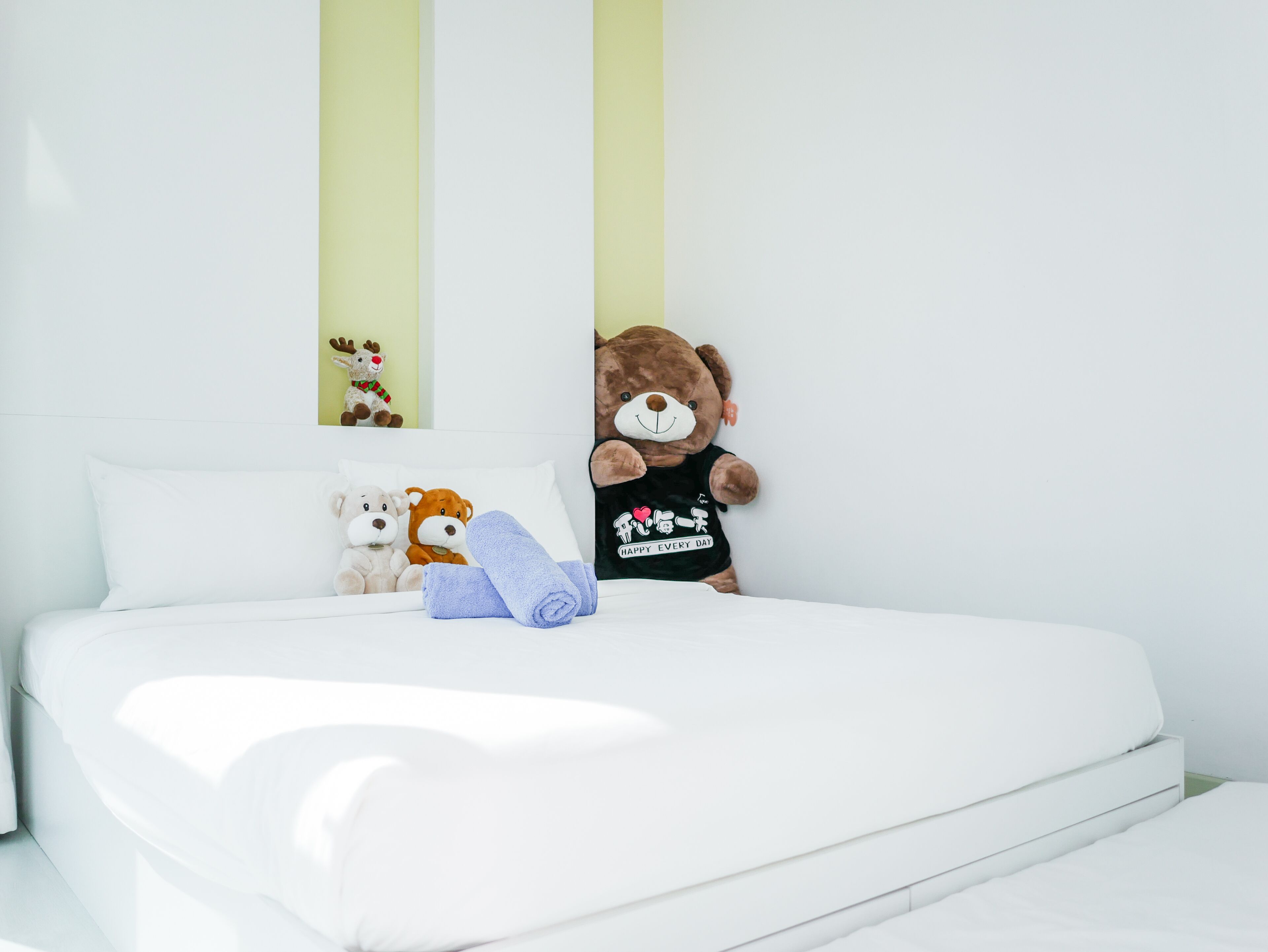 Ein ordentlich gemachtes Bett mit weißer Bettwäsche, einem Teddybären und zwei Kuscheltieren auf den Kissen.