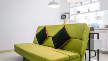 A green sofa with black cushions in a modern, well-lit room with white walls and a large window.