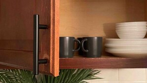 A wooden cabinet with a black handle, a shelf with black mugs and stacked white plates. - Moroccan Lover's Oasis: 2BR/ 2BA Great for Large Groups and Families (Queens)