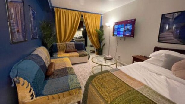 A hotel room with a sofa, a bed, a TV, and a small table. - Moroccan Lover's Oasis: 2BR/ 2BA Great for Large Groups and Families (Queens)