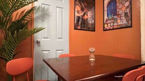 A dining area with a wooden table and four orange chairs. There is a potted plant to the left and two framed pictures on the wall. - Moroccan Lover's Oasis: 2BR/ 2BA Great for Large Groups and Families (Queens)