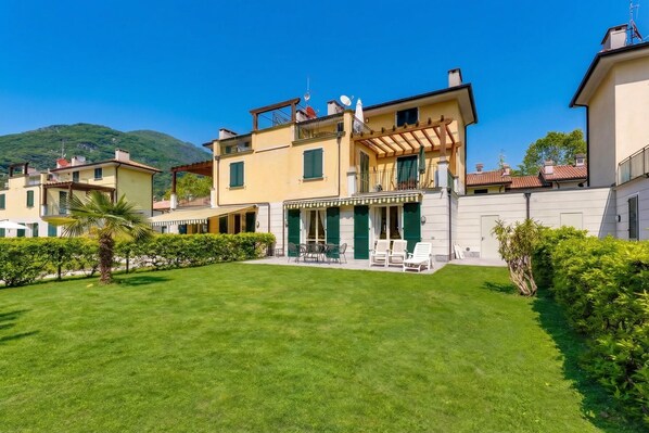 A multi-story residential building with a well-maintained lawn, outdoor seating, and a mountain backdrop.