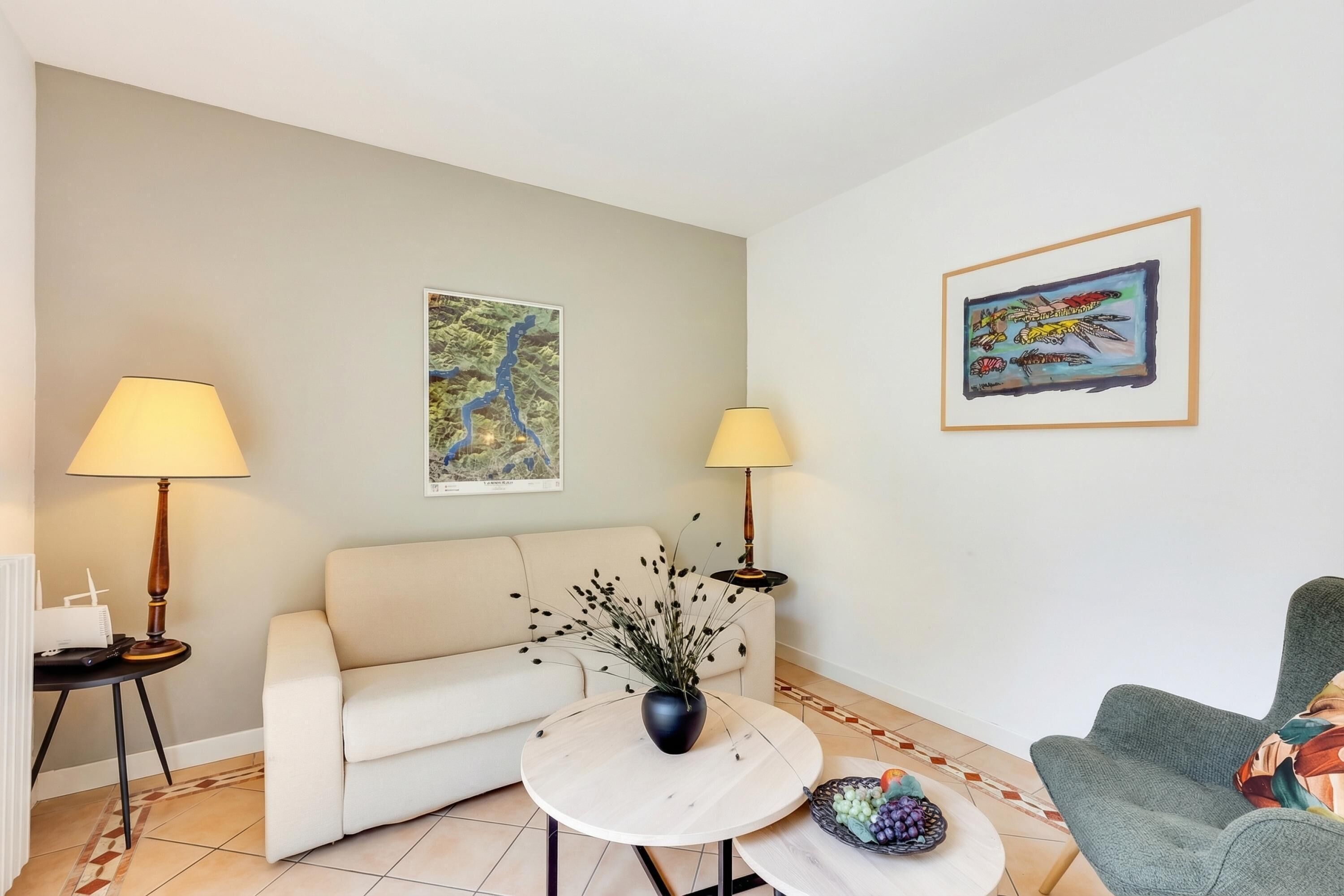 Ein Wohnzimmer mit einer Couch, zwei Lampen, einem Couchtisch und zwei gerahmten Kunstwerken an den Wänden.