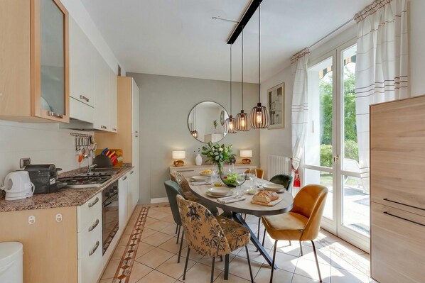 Une cuisine moderne avec un coin repas, une grande fenêtre avec des rideaux et une vue sur la verdure à l’extérieur.