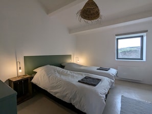 Une chambre avec deux lits, une table de chevet avec une lampe, une fenêtre donnant sur un beau paysage et un luminaire suspendu.