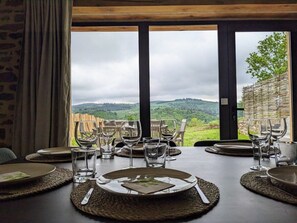 Une table à manger dressée pour six personnes, avec une vue imprenable sur un vignoble et des collines.