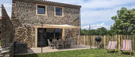 A stone building with a patio, outdoor seating, and a barbecue grill.