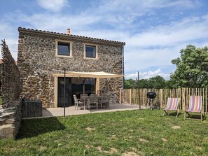 A stone building with a patio, outdoor seating, and a barbecue grill.