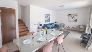 Una sala de estar moderna con una mesa de comedor de vidrio, sillas rosadas, un sofá azul y una escalera que conduce a otro nivel.