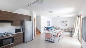 Una cocina moderna con horno empotrado, microondas y refrigerador. Hay un comedor con mesa de vidrio y sillas rosas.