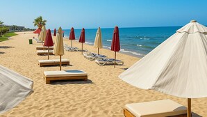 Ein Strand mit Reihen von Liegestühlen und Sonnenschirmen, einem wolkenlosen, blauen Himmel und dem Meer im Hintergrund.
