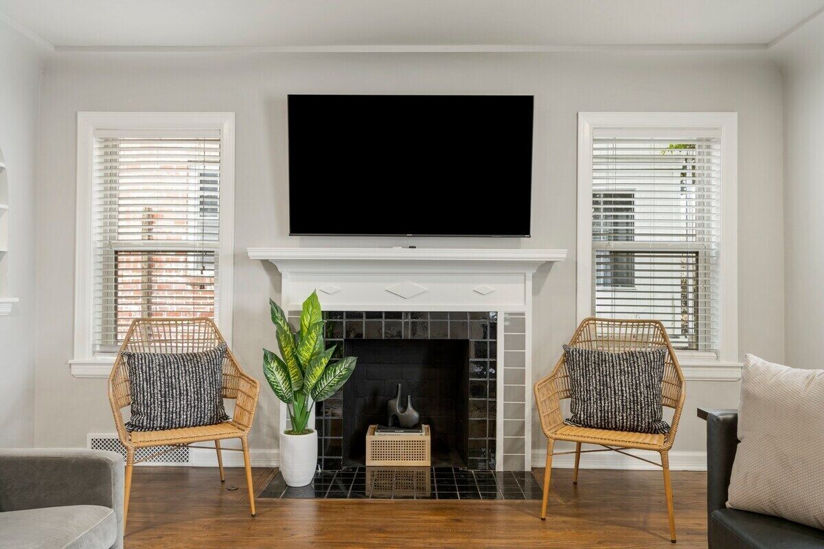 Una sala de estar con chimenea, dos sillones de mimbre, un sofá y un televisor de pantalla plana sobre la chimenea.