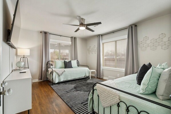 A bedroom with a bed, a desk, a chair, a ceiling fan, and a window with blinds. - Breezy Billiards @TulsaExpo (Tulsa)