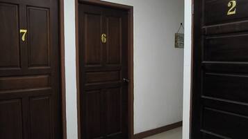 A hallway with three wooden doors, each marked with a number. The hallway has white walls and a tiled floor.