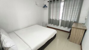A small, clean room with a single bed, a wooden nightstand, a wall-mounted shelf, and a window with curtains. - Natol Homestay - Kenyalang Park  (Kuching)