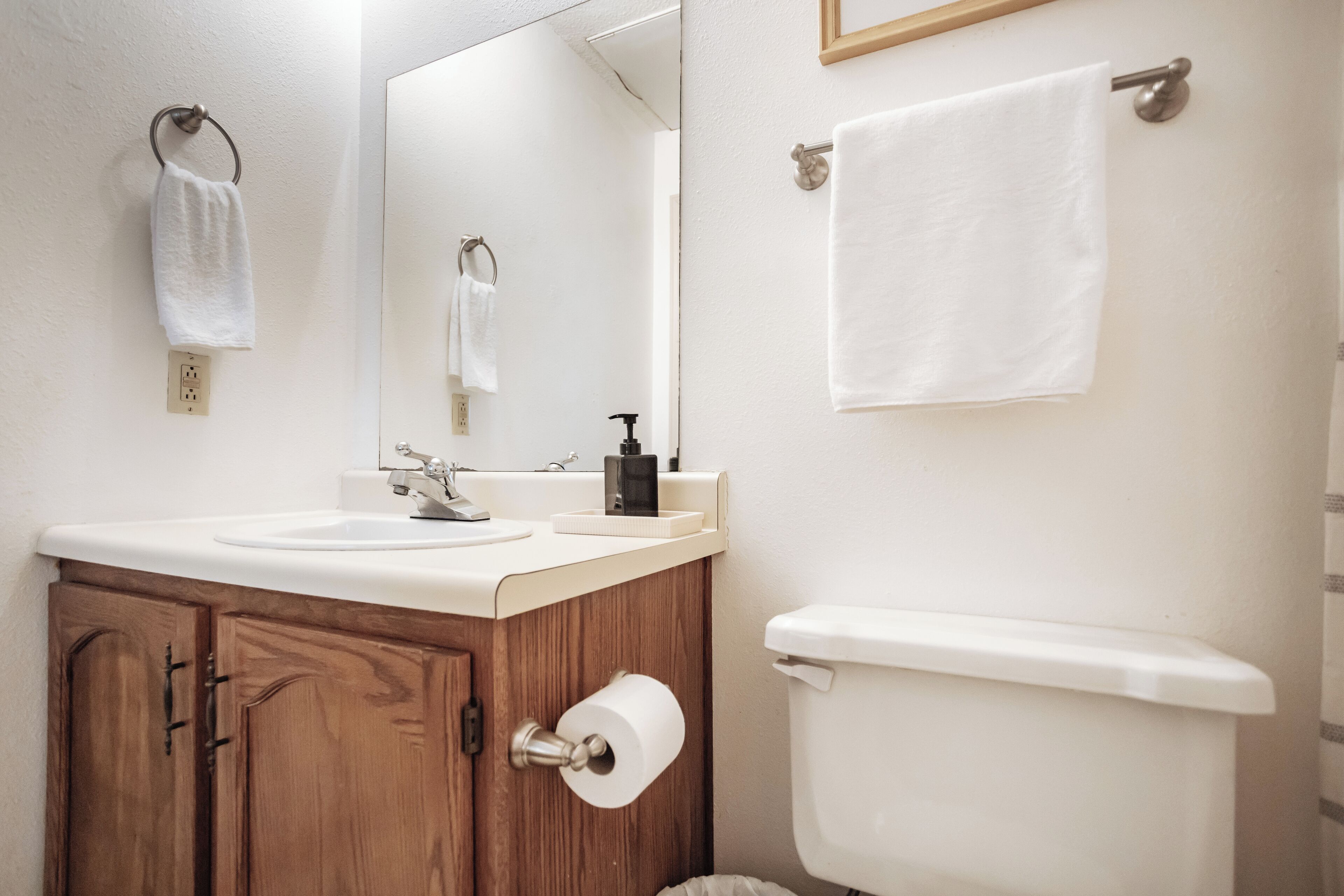 Un baño con tocador de madera, un lavabo, un espejo, un inodoro y dos toallas colgadas en barras.