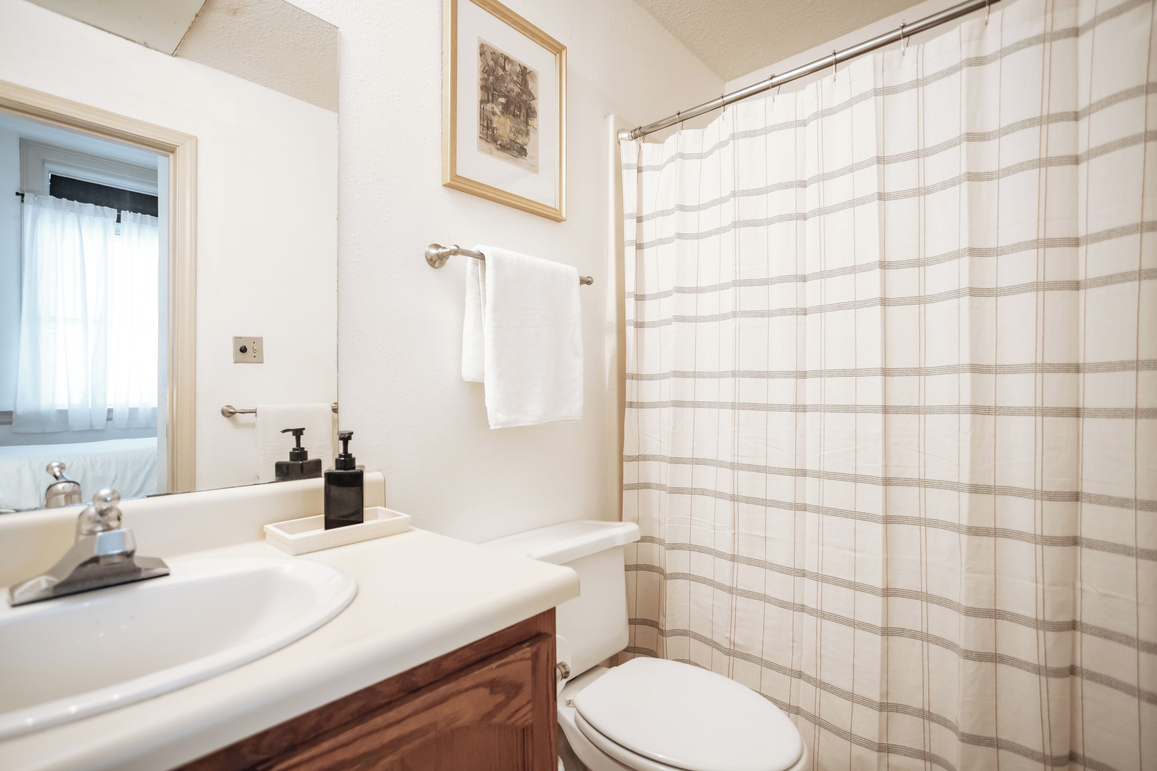 Ein Badezimmer mit einem weißen Waschbecken, einer Holz-Waschkommode, einer weißen Toilette und einer Duschvorhang mit Schachmuster.