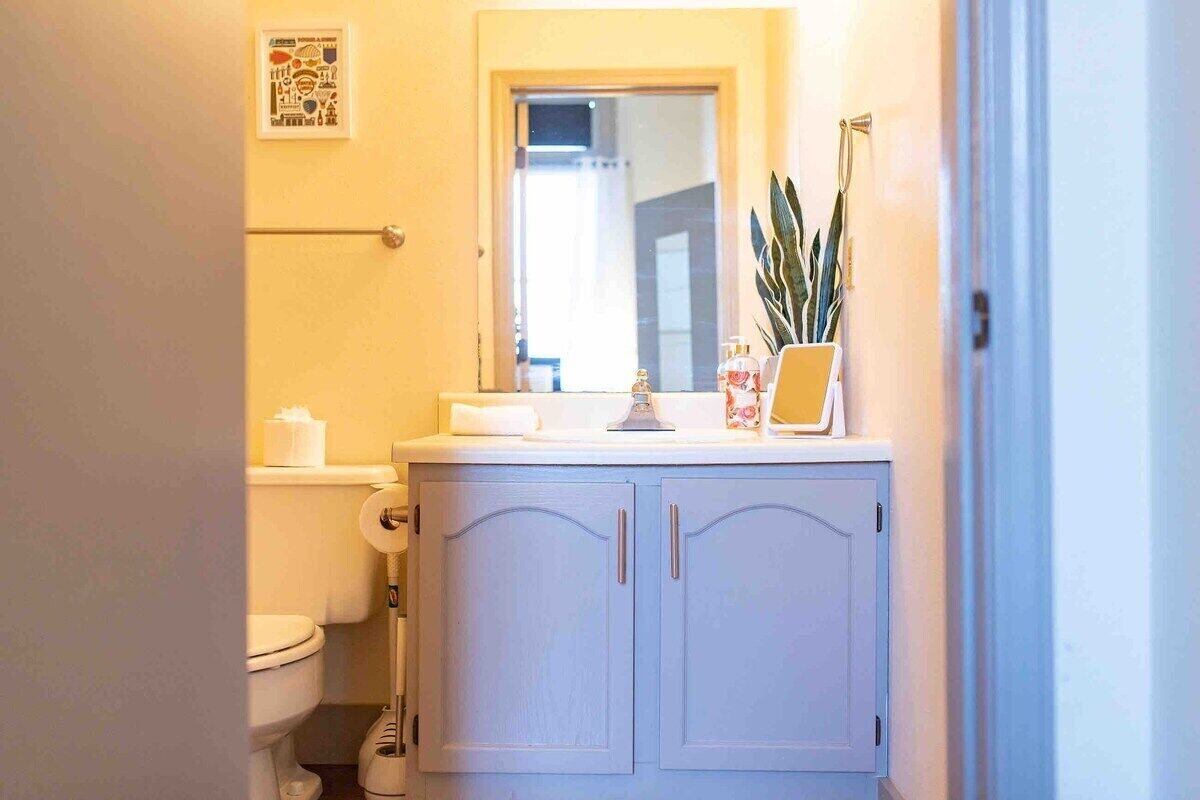 Un baño con inodoro, lavamanos con espejo y una planta en la encimera.