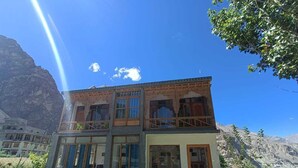 A two-story building with a balcony, surrounded by mountains and a garden with various flowers. - Hotel The Stone Palace (Leh)