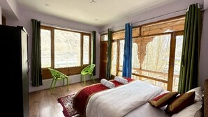 A bedroom with a large bed, a green chair, and a window with curtains. - Hotel The Stone Palace (Leh)