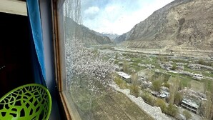 A view from a window of a mountainous landscape with a river, buildings, and a chair. - Hotel The Stone Palace (Leh)