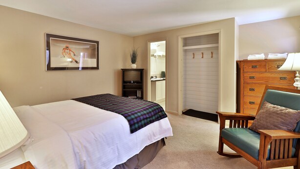 A bedroom with a bed, a chair, a dresser, and a television. - The Birch Ridge: Mission Room #4 - Queen Suite in Killington, Vermont (Killington)