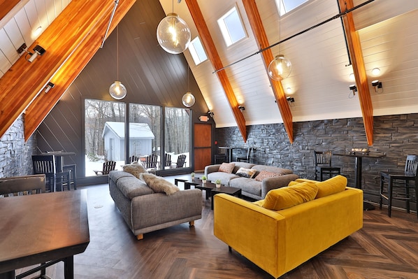 A spacious loft-style living area with high ceilings, exposed wooden beams, and large windows.