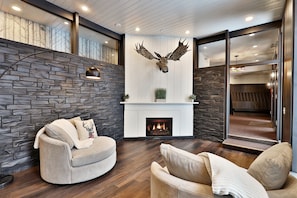 A modern living room with a stone wall, a fireplace, a mounted deer head, and a cozy seating area.
