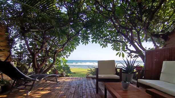 Une terrasse en bois avec vue sur l’océan, une chaise, un canapé et une plante en pot.