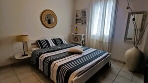 Une chambre à coucher bien rangée, avec un lit, une lampe de chevet, un miroir et une étagère où sont posés des objets personnels.