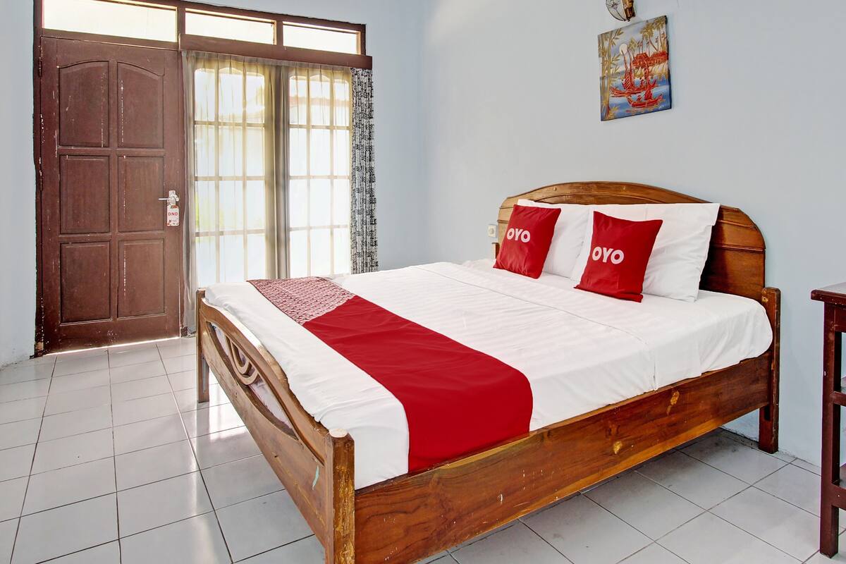 A wooden bed with white and red bedding, a wooden headboard, and a red throw blanket.