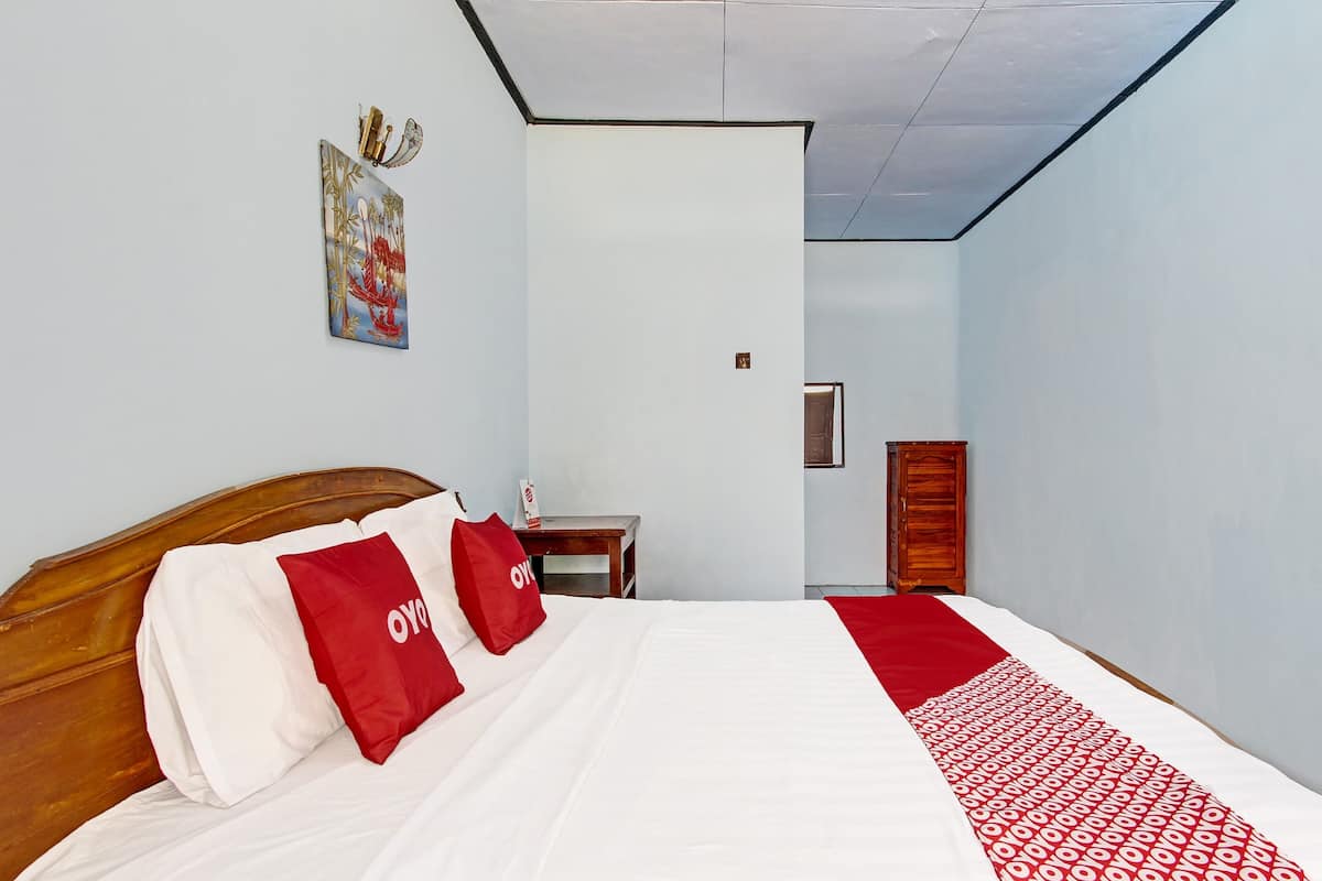 A hotel room with a neatly made bed, a wooden headboard, a nightstand, a wardrobe, and a wall-mounted artwork.