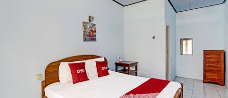 A bedroom with a wooden bed, white and red bedding, a small bedside table, a wooden wardrobe, and a wall-mounted picture.