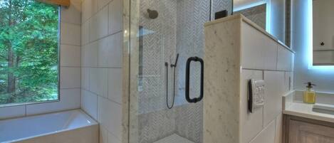 A modern bathroom with a glass-enclosed shower, a window with a view of trees, and a wooden vanity.