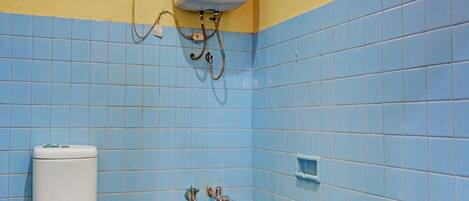 Un baño con azulejos azules, un inodoro blanco y una bañera azul.