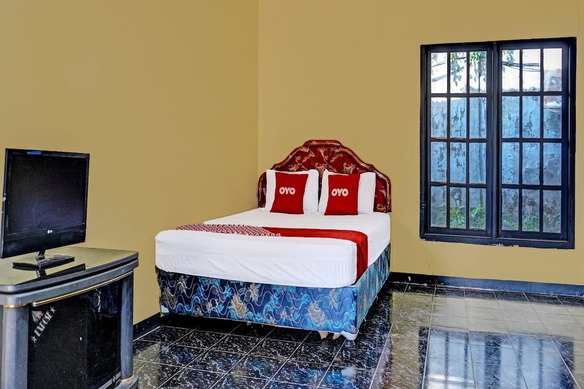 A room with a bed, a television, and a window.