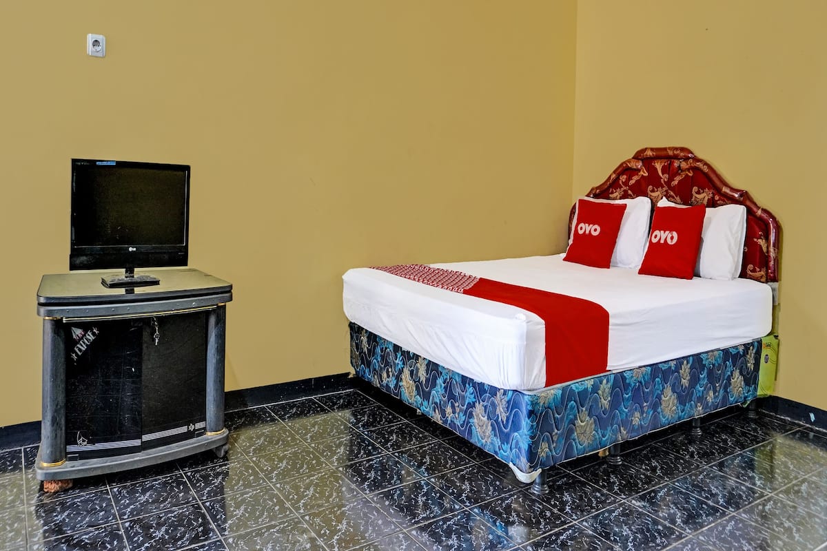 A hotel room with a bed, a television on a stand, and a tiled floor.