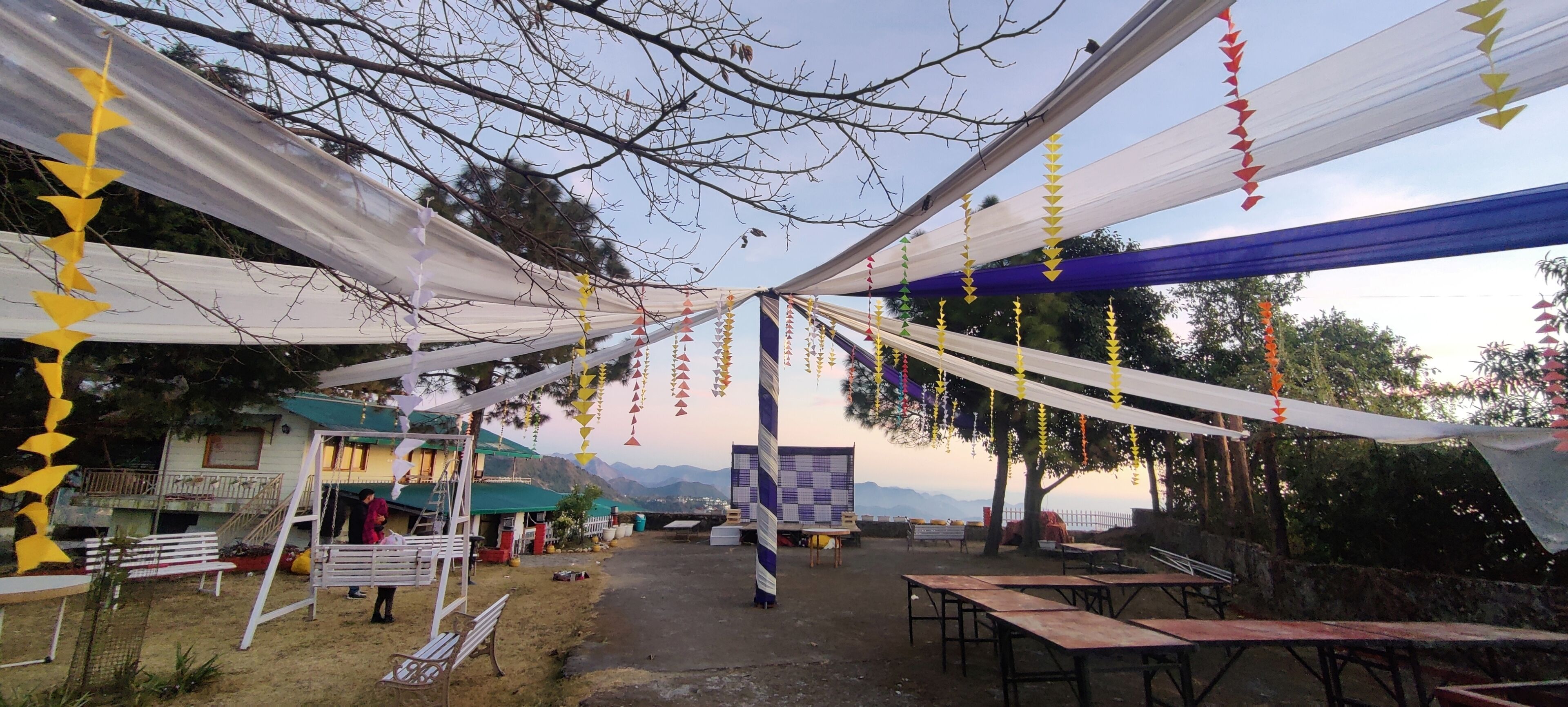 An outdoor event space with tables and chairs, a white tent, and colorful hanging decorations.