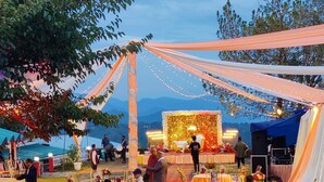 An outdoor event with tables and chairs arranged on a carpeted path, surrounded by trees and a scenic backdrop. - Saiva Hill Resort (Dehradun)