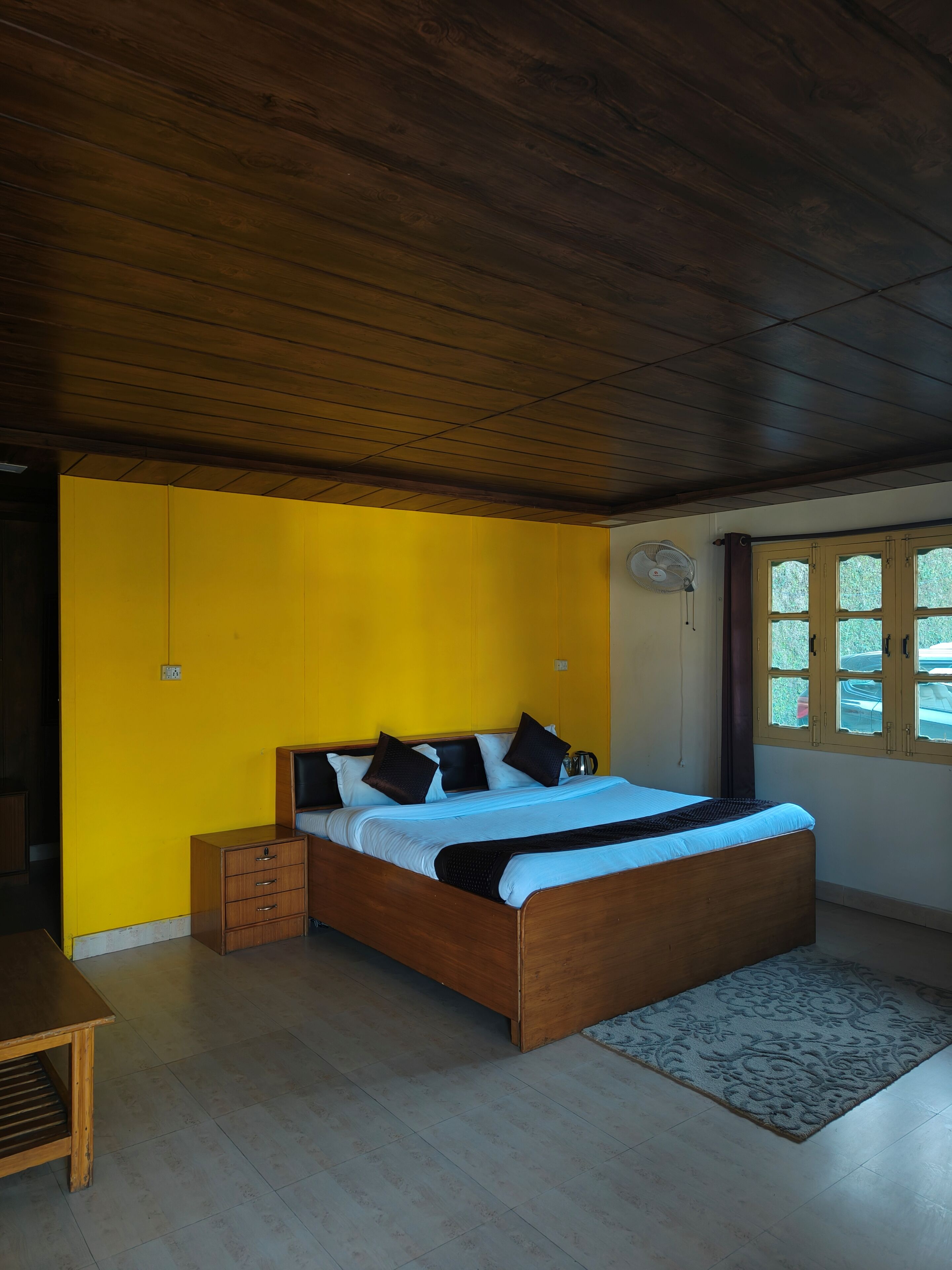 A bedroom with a wooden bed, a yellow wall, and a window with curtains.