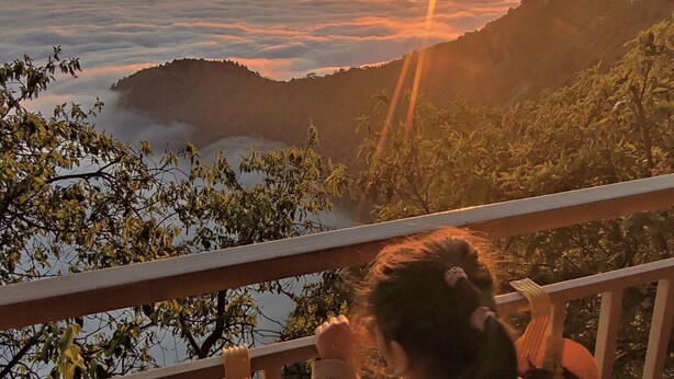 A child on a wooden deck overlooking a mountainous landscape during sunset. - Saiva Hill Resort (Dehradun)