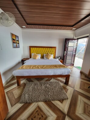 Une chambre avec un plafond en bois, un lit doté d’une tête de lit jaune, une grande fenêtre et une vue sur l’extérieur.