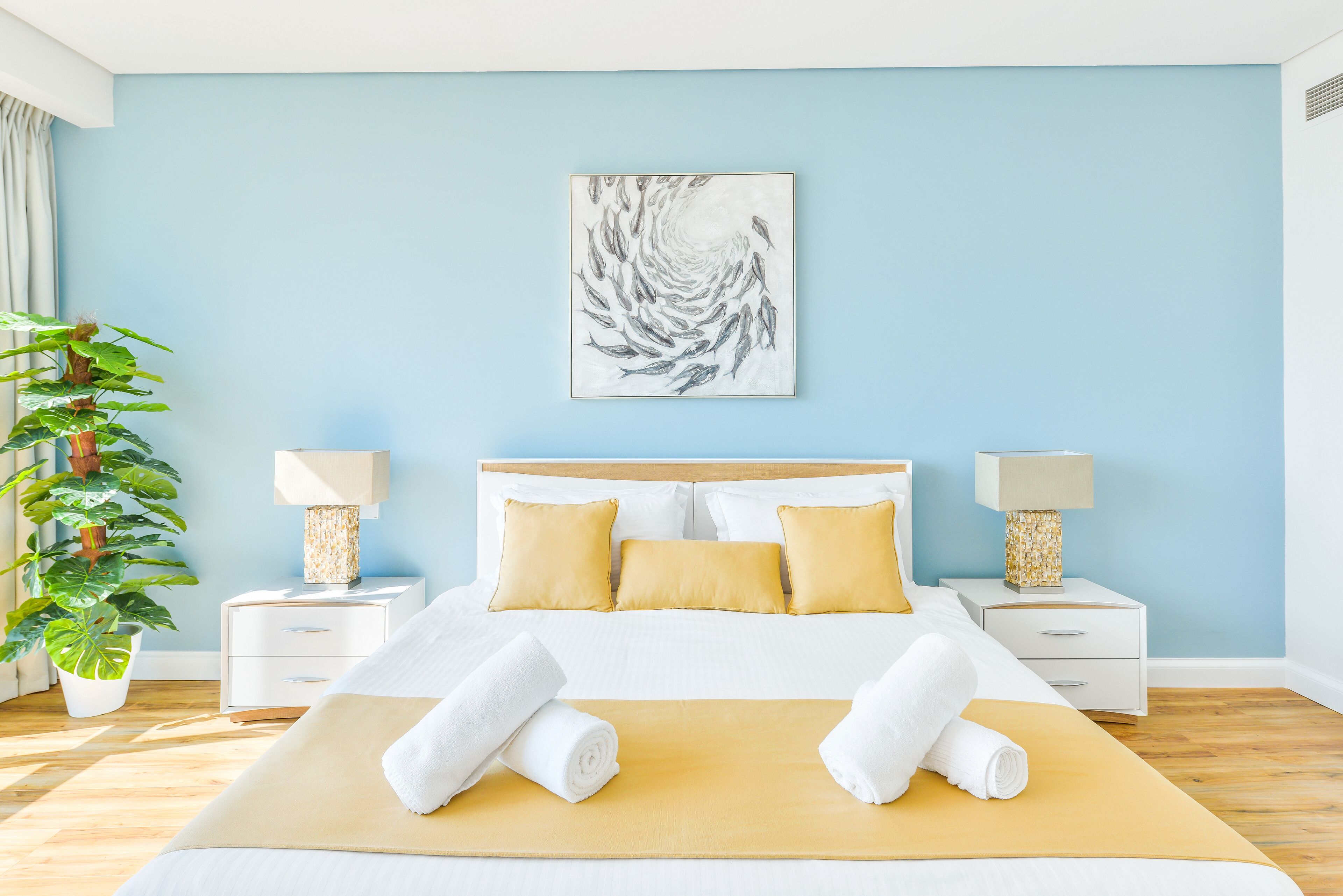 A modern hotel room with a large bed, two bedside tables with lamps, a large window, and a potted plant.