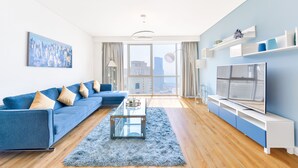 A modern living room with a blue sofa, a glass coffee table, and a TV on a white stand. - Luxury JBR - Al Fattan Full Sea View - Free Beach Resorts Access (Dubai)