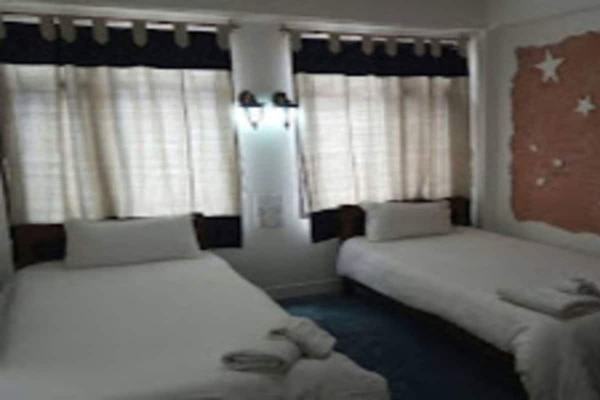 A room with two single beds, a large window with curtains, and a wall with a crescent moon and stars.
