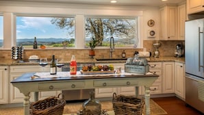 A kitchen with a view of the countryside, a farmhouse sign, and a rustic table with baskets and jars. - Picturesque Panoramic Vineyard Views From Home and Hot Tub, Pet Friendly, Private, Fire-Pit, BBQ (Newberg)