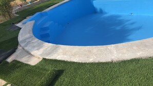 Piscina con revestimiento azul, rodeada por un muro de piedra y una zona verde.