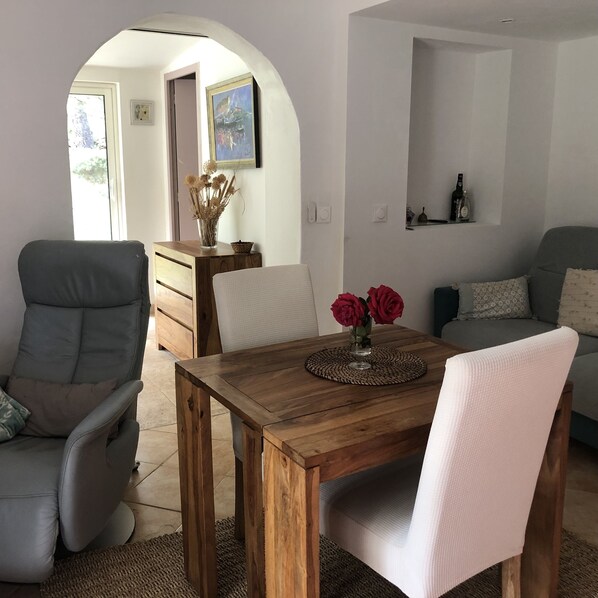 A dining area with a wooden table, chairs, and a vase with red flowers.