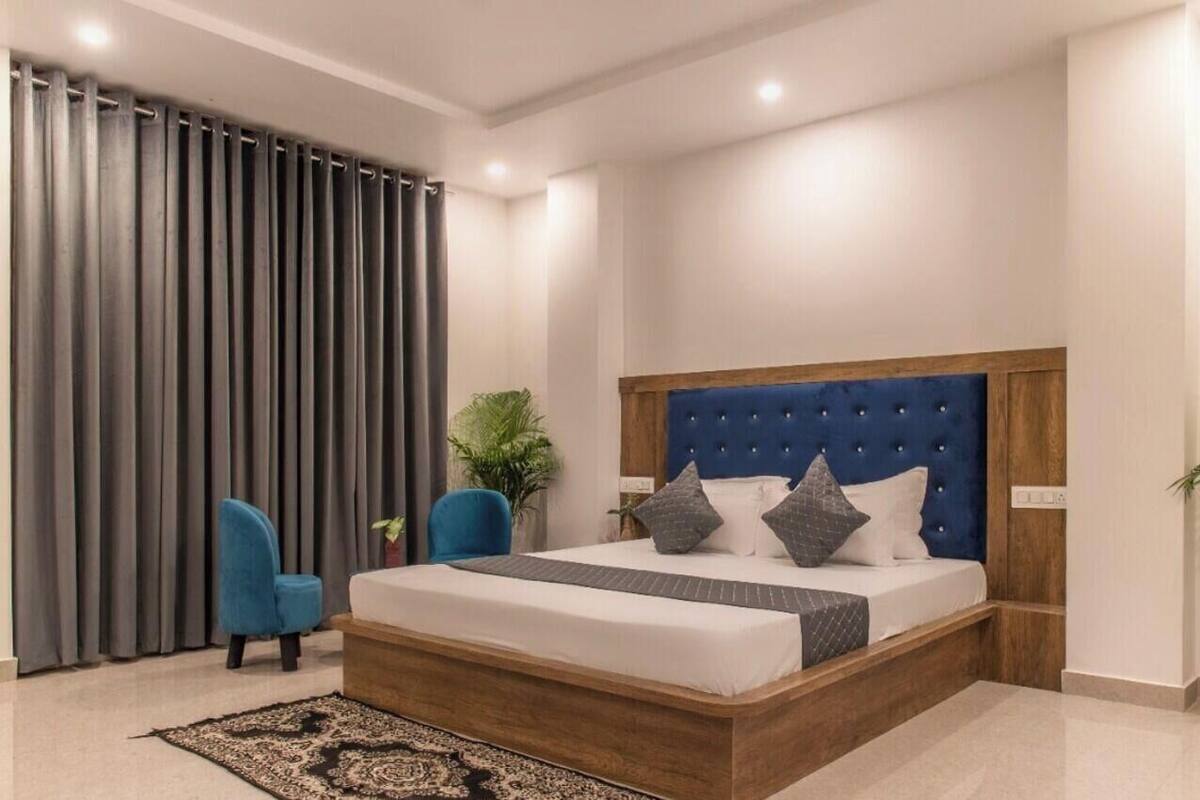 Een moderne slaapkamer met een groot bed, een blauw gestoffeerd hoofdeinde, een houten nachtkastje, een blauwe stoel en een potplant.